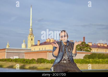 Young man is spreading his hands in frustration on the background of historic architecture of Saint-Petersburg, Russia. Stock Photo