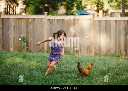A happy child plays barefoot with a chicken in her backyard garden Stock Photo
