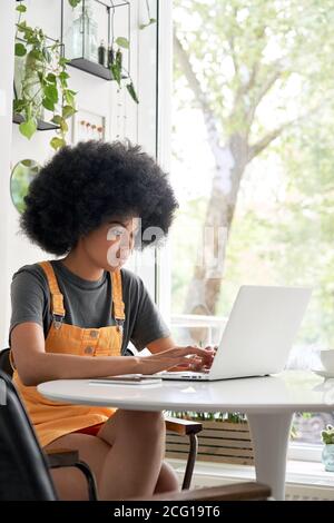 Young African woman student using laptop sitting at table at home, in cafe. Stock Photo