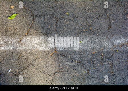 Bumpy road with one painted white line marking and big chunks of gray cracked asphalt. Rough journey or travel concept Stock Photo