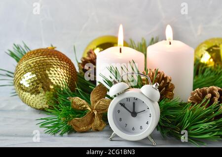 Christmas composition. Two candles and pine branches with cones and a white alarm clock. Stock Photo