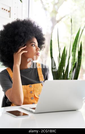 Thoughtful African lady looking through window sitting at cafe table use laptop. Stock Photo