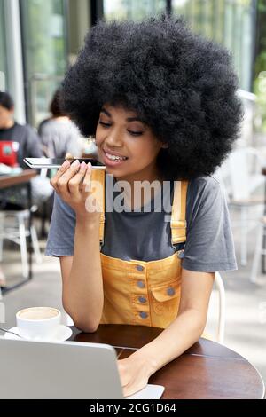 African woman using mobile voice recognition assistant sitting in outdoor cafe. Stock Photo