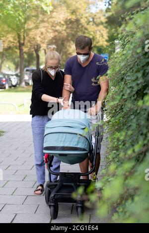 Worried young parent walking on empty street with stroller wearing medical masks to protect them from corona virus. Social distancing life during Stock Photo