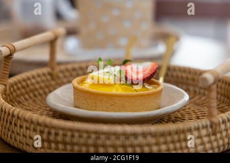 Lemon and strawberry tarts are placed on a white plate in rattan basket. Stock Photo