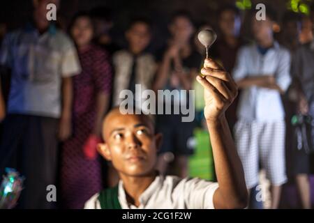 YANGON, MYANMAR DECEMBER 3, 2016 : Street performer in Maha Bandula Park with spinning top performs for crowd at night. Stock Photo