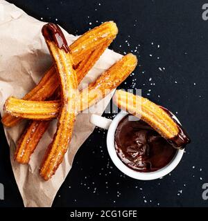 Churros with sugar dipped in chocolate sauce on a black background. Churro sticks. Fried dough pastry, top view Stock Photo