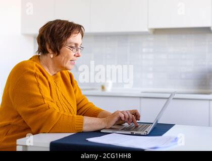 Smiley elder woman working with laptop at home. Distant working concept. Stock Photo