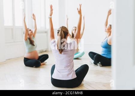 Group of pregnant women in sports uniforms with coach doing gymnastic in bright studio Stock Photo