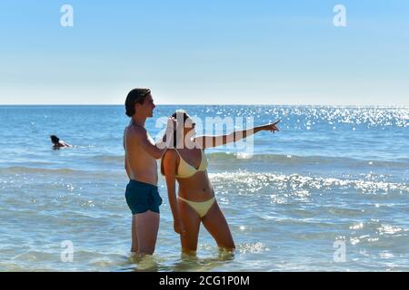 Young woman pointing away and young man taking off his glasses to check. New holidays and couples concept. Stock Photo