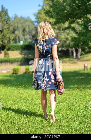 Beautiful blond woman in the park holding her shoes in hand Stock Photo