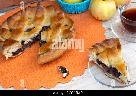home cooking, pie, a piece of apple pie with cherry and walnuts, a cup of tea, apples in a basket and walnuts on the table Stock Photo