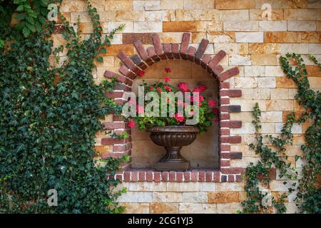 Wall flower pot with pink flower plants, outdoor decorative. Stone wall decorated with flowers. Wall of the building is covered with ivy Stock Photo