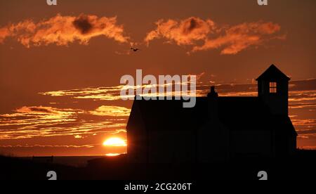 The sun rises behind the Watch House Museum at Seaton Sluice, on the North East coast of England. Stock Photo