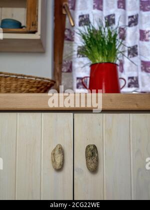Wooden kitchen in vintage style with chives in red pot on background. Detail of handle made from stone. Stock Photo