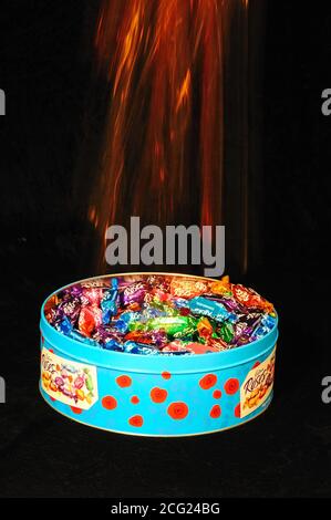 Chocolates being dropped into a tin against a black background Stock Photo