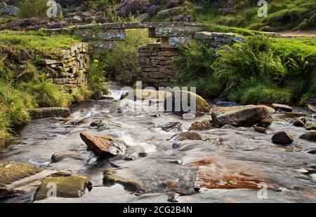 The waters of South Dean Beck flowing under a stone footbridge, on Haworth Moor, in Bronte country, Yorkshire, UK Stock Photo