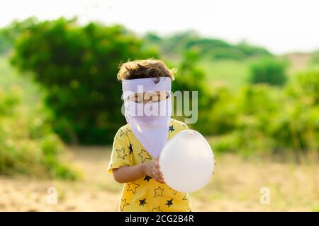 A little cute baby wearing a home made white full face mask and holding a white balloon in his hands Stock Photo