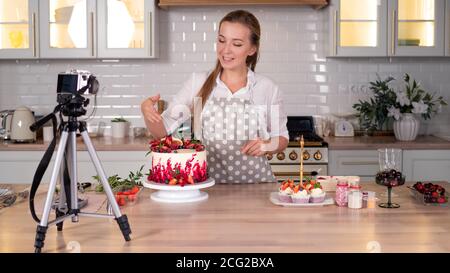 Blogger pastry chef makes a video lesson about cooking a cake, young woman in an apron at home in the kitchen. Online broadcast. Stock Photo