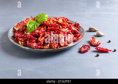 Sun-dried tomatoes in a gray plate with a sprig of basil, garlic and peppers on a gray background. Horizontal orientation. Stock Photo