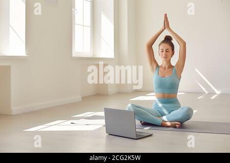 Female yoga coach showing asana in front of laptop during online video lesson with client Stock Photo