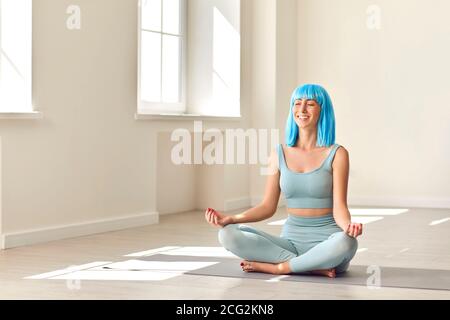 Smiling young woman sitting in lotus position and meditating sitting on sports mat. Stock Photo