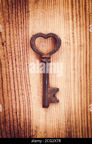 Old rusty vintage key in the shape of a heart, wood background. Love and Valentine's day greeting card Stock Photo