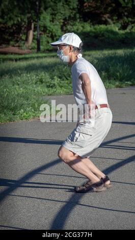 A nimble senior citizen does deep knee bends warming up for an exercise walk. In a park in Queens, New York City. Stock Photo