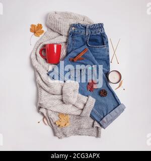 Autumn flat lay composition. Jeans, knitted sweater, red cup and yellow leaves on white table, top view Stock Photo