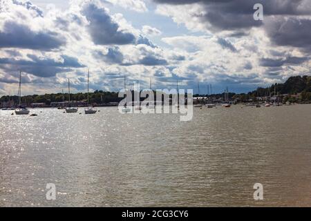 The late afternoon sun breaks through the storm clouds and sparkles on the water amongst moored yachts at Upnor on River Medway, Kent, UK Stock Photo