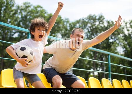 Dad and son watching football game on stadium and screaming Stock Photo