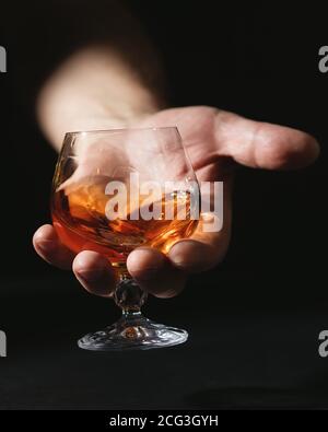 Cognac glass in man's hand. Bright amber drink. Dark background Stock Photo