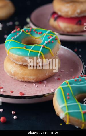 Donuts with multicolored icing sugar with various sugar sprinkles in stacks on pink plates. Sweet food background Stock Photo