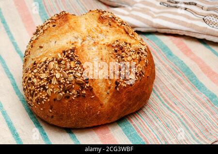 Freshly baked whole grain loaf of bread sprinkled with seeds of flax, sesame, sunflower seeds on linen towel. Healthy eating concept. Home baking Stock Photo