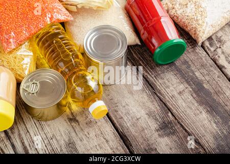 Donations food. Set of staple products raw cereals canned food, grocery pasta on wooden table. Donate help, delivery foodstuff during covid quarantine Stock Photo