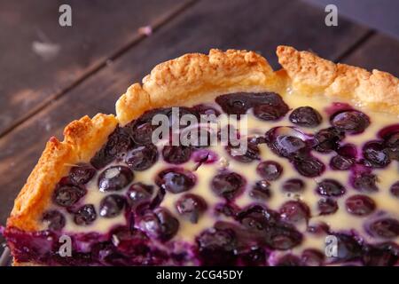Edge of rustic shortbread pie with blueberries in sour cream filling on a wooden background with piece cut off. Stock Photo