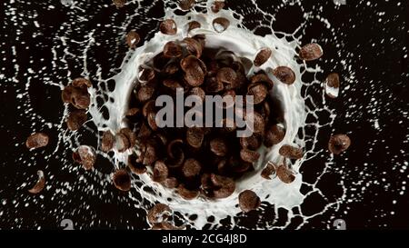 Freeze motion of rotating cereal pieces with milk splash, isolated on black background. Flying food concept, healthy eating. Stock Photo