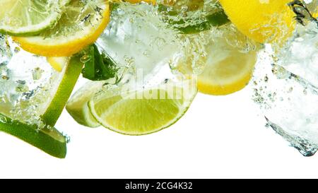 Lemon and lime slices with ice cubes and leaves falling deeply under water isolated on white background Stock Photo