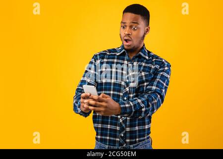 African Man Holding Cellphone Reading Wow News On Yellow Background Stock Photo