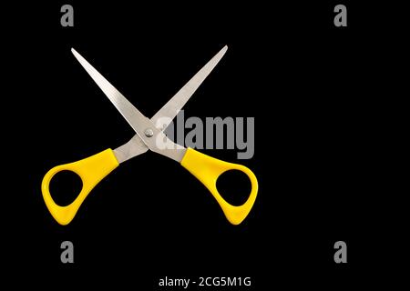 Yellow plastic handled open stainless steel scissors on a black background with copy space Stock Photo
