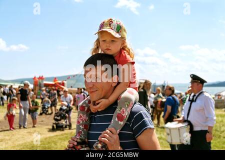 Father carries daughter on his shoulders during the music and ethnic festival Karatag on the background of people. Stock Photo