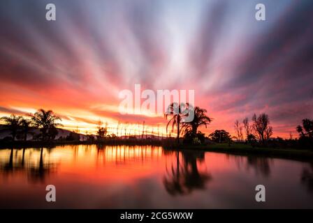 Clouds on fire during golden hour with moody sky, reflections on surface of farm dam