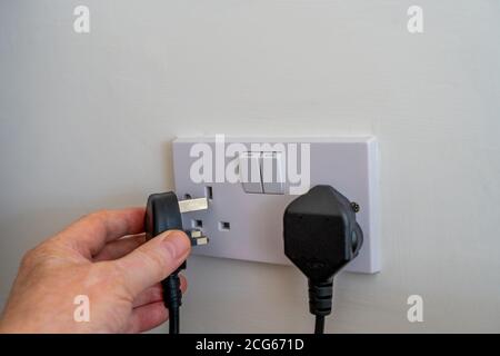 Selected Focus Plugging in a United Kingdom ( British) three pin fused plug into a double wall socket connecting an appliance to electrical power 240v Stock Photo