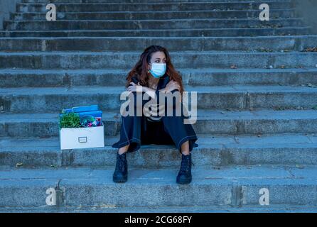 COVID-19 lay off and unemployment. Depressed business woman with face mask outside office with personal staff box feeling hopeless after losing job du Stock Photo