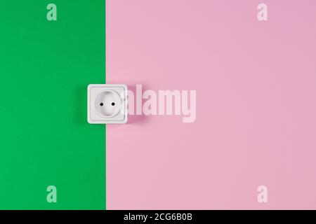 White electrical socket on light pink and green color background. Stock Photo