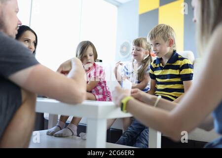 Adults and children are sitting around table on which playing cards are located boy looks thoughtfully at adults Stock Photo