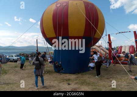 Children with parents ride on an inflatable swing on the Playground during the musical festival Karatag on the shore of Large lake Stock Photo