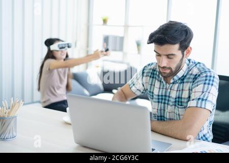 Man working from home while a woman plays a computer game behind him Stock Photo
