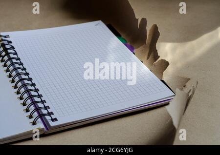 Open spring-bound notebook in sunlight. New diary with blank pages on torn wrapping paper. Side view at an angle. Selective focus. Stock Photo
