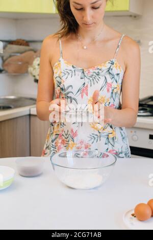Woman standing in kitchen sifting flour into a bowl Stock Photo